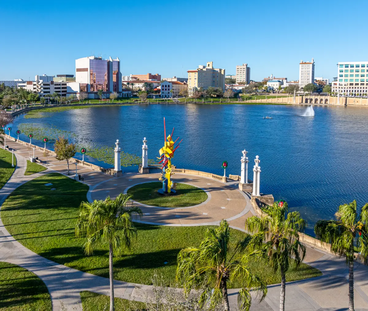 Cityscape with lake and colorful sculpture.