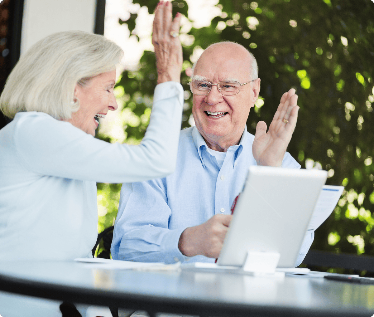 Elderly couple high-fiving at outdoor table.