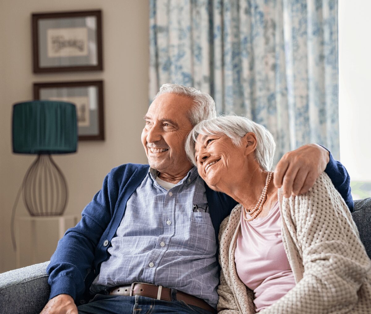 Elderly couple smiling on cozy living room sofa.
